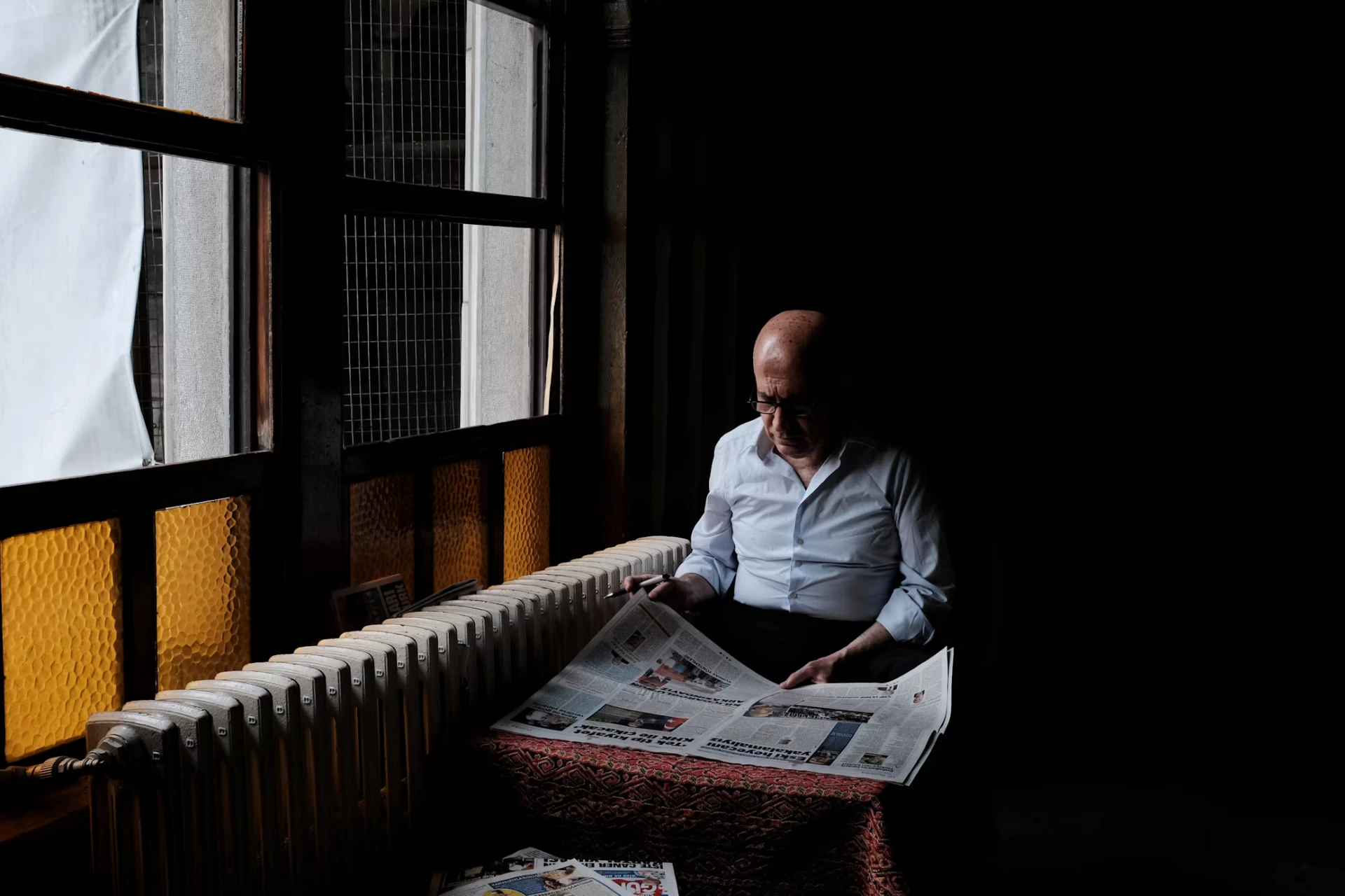 Un homme lit le journal près d’une fenêtre aux vitres ambrées